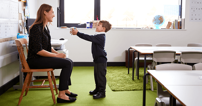 a little kid offering a gift to his female teacher in a classroom 