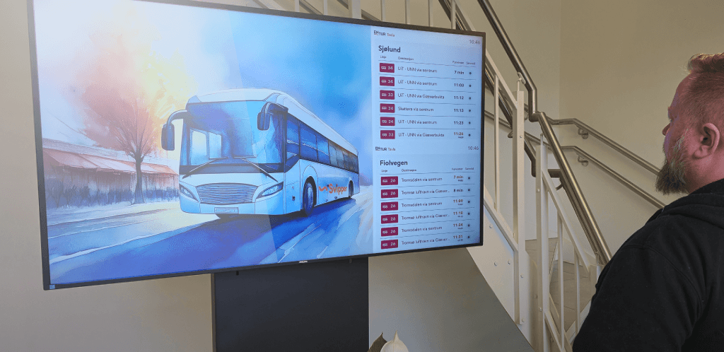 a digital screen showing a schedule next to a bus and a man looking at the screen