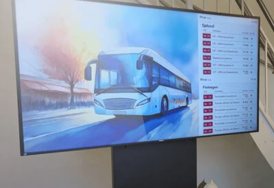 a digital screen showing a schedule next to a bus and a man looking at the screen