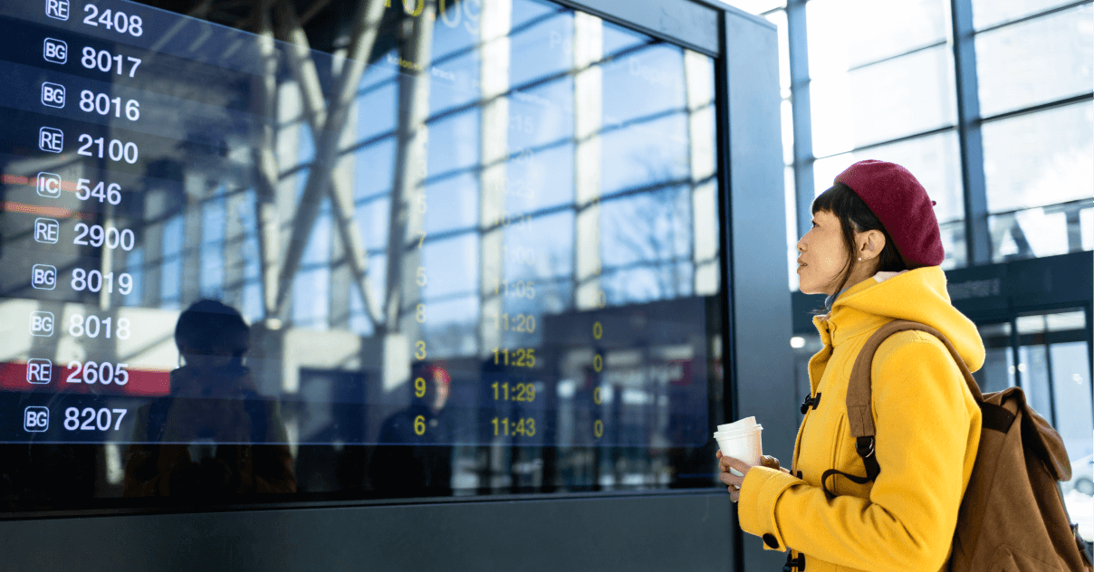 A woman at an airport looking at a large screen displaying flight information.